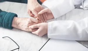 Mãos de fisioterapeuta segurando com cuidado as mãos de uma senhora idosa