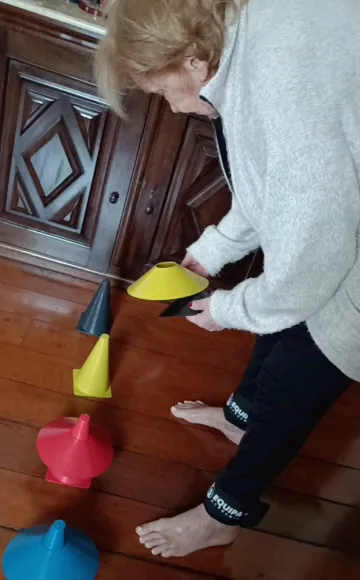 Idosa se abaixando para pegar cones coloridos no chão em treino de equilíbrio