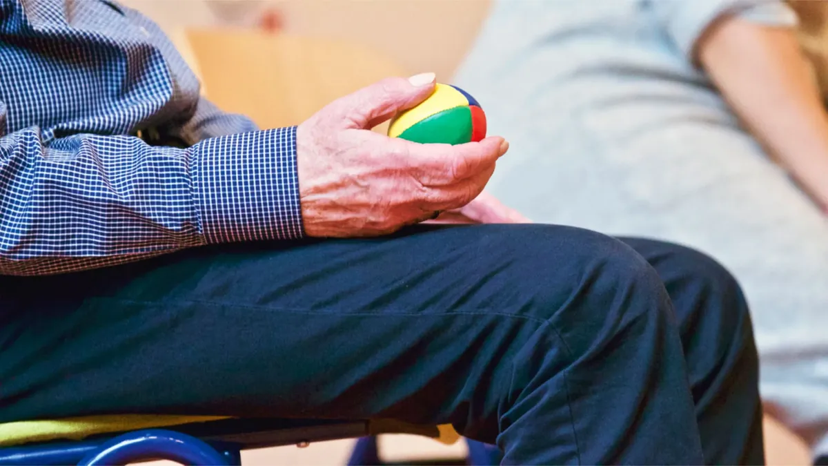 Mão de um idoso apertando uma bola colorida em exercício de coordenação