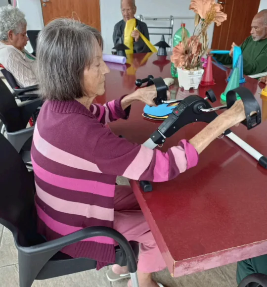 Idosa exercitando os braços com pedalinho sobre a mesa