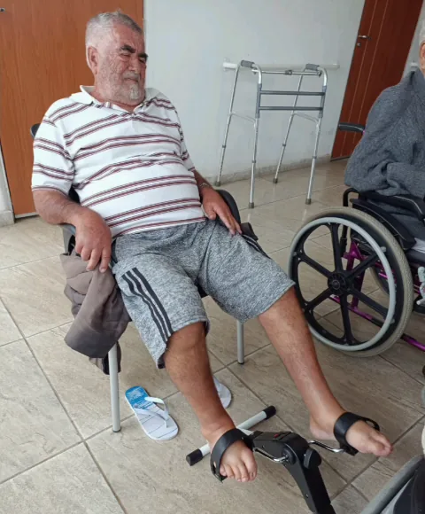 Idoso sentado pedalando um mini cicloergômetro com os pés